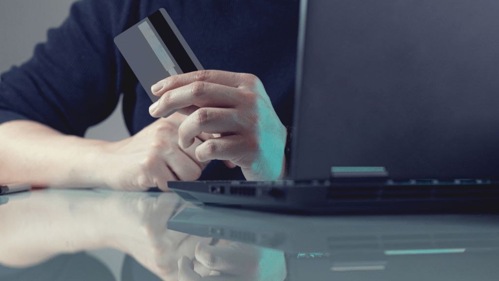 man holding credit card beside laptop