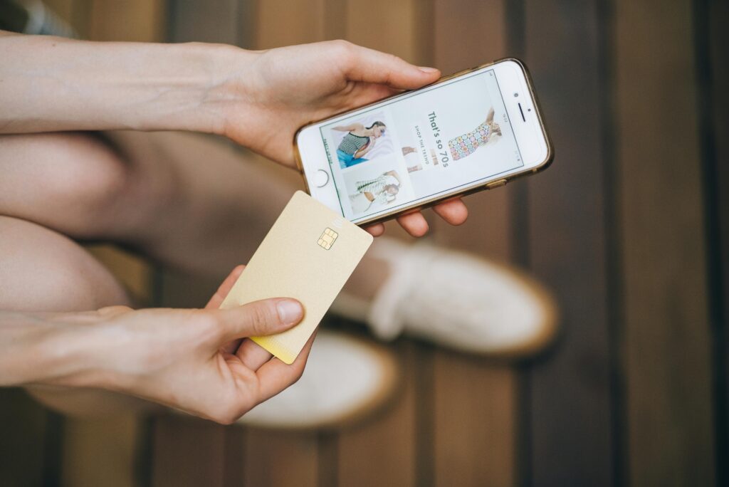 Hands holding smartphone and credit card for online shopping on a wooden floor.